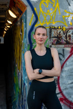 Load image into Gallery viewer, model with black crop top stands near graffiti painted wall

